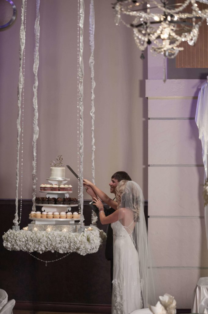 Couple-cutting-cake-and-cupcakes-on-hanging-table_sml-copy-681x1024